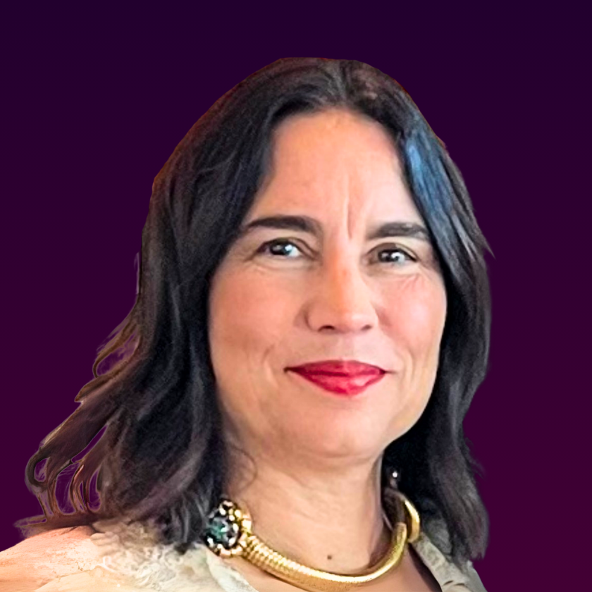 A closed-mouth portrait of Nicola Miner sits on a dark purple gradient background. She has mid-length dark brown hair and wears red lipstick. Around her neck is a thick gold necklace and she wears a cream top.